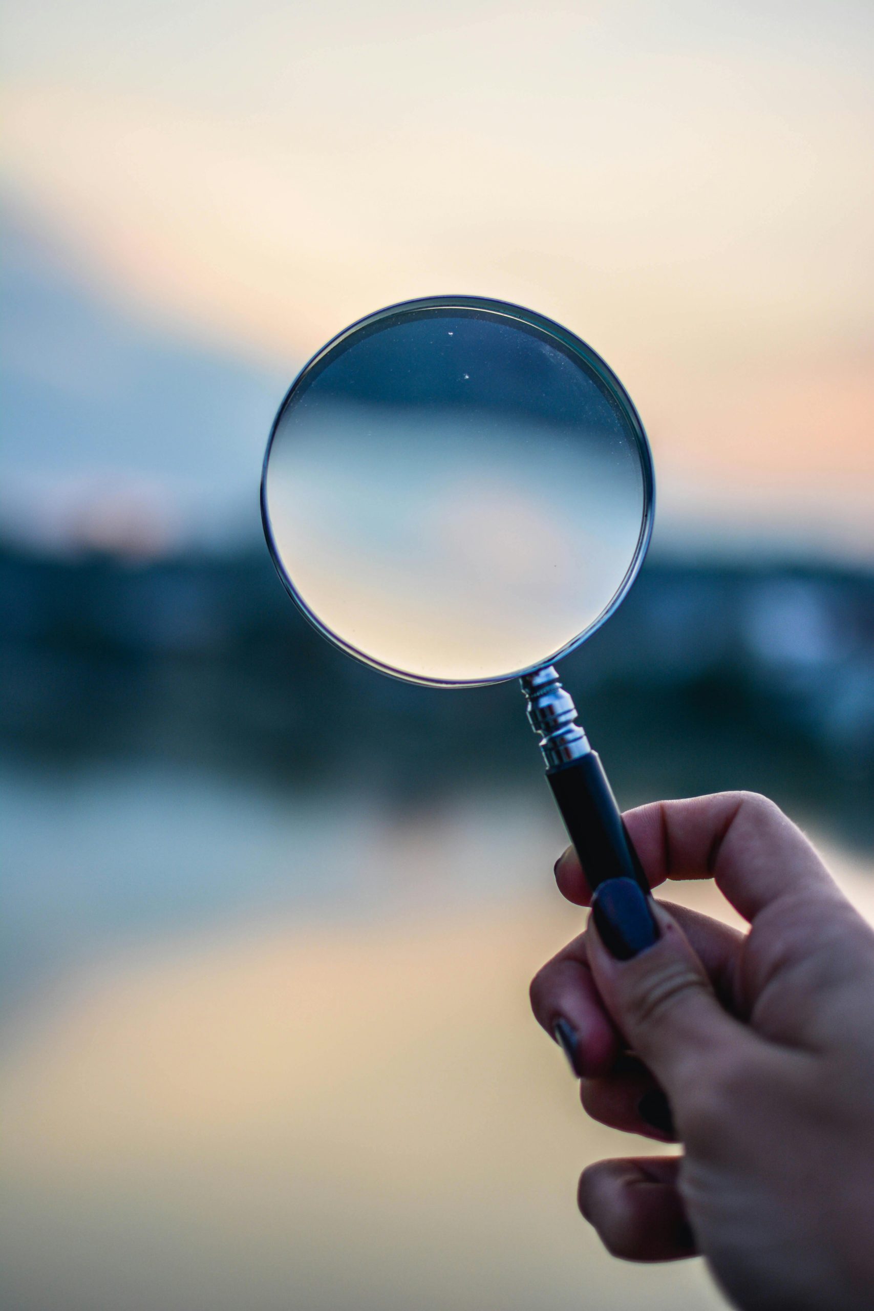 Hand holding a magnifying glass outdoors